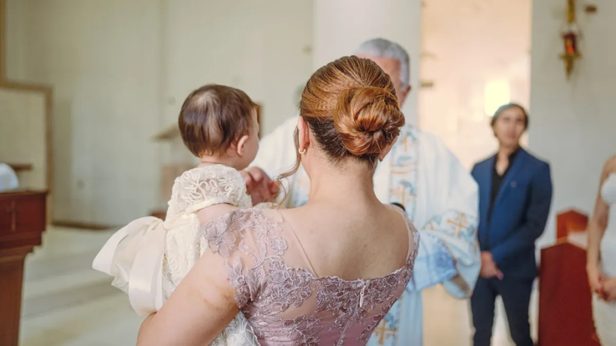 Mother holds baby during baptism ceremony with priest