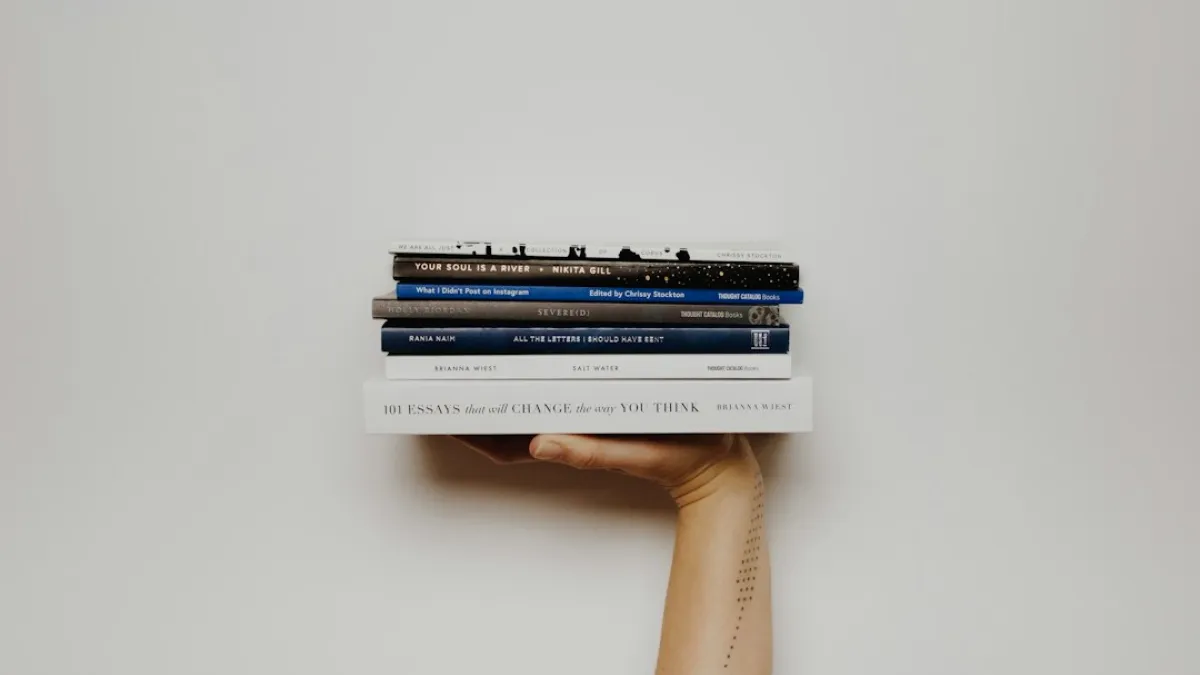 Woman with a tattoo holding up a stack of books.