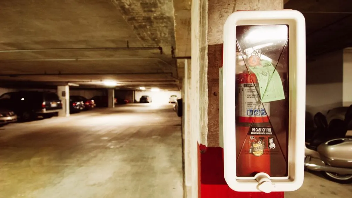 Fire extinguisher in an underground parking garage with parked cars.