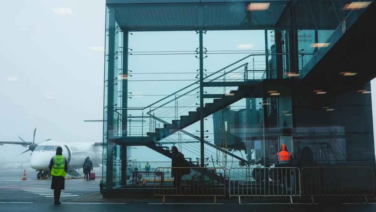 Passengers boarding an airplane at Riga Airport amidst fog, showcasing modern airport architecture.