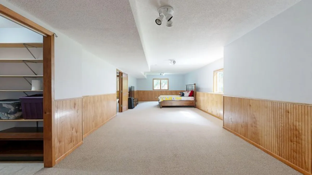 Empty basement room with wooden paneling and carpet, offering ample space for various uses.