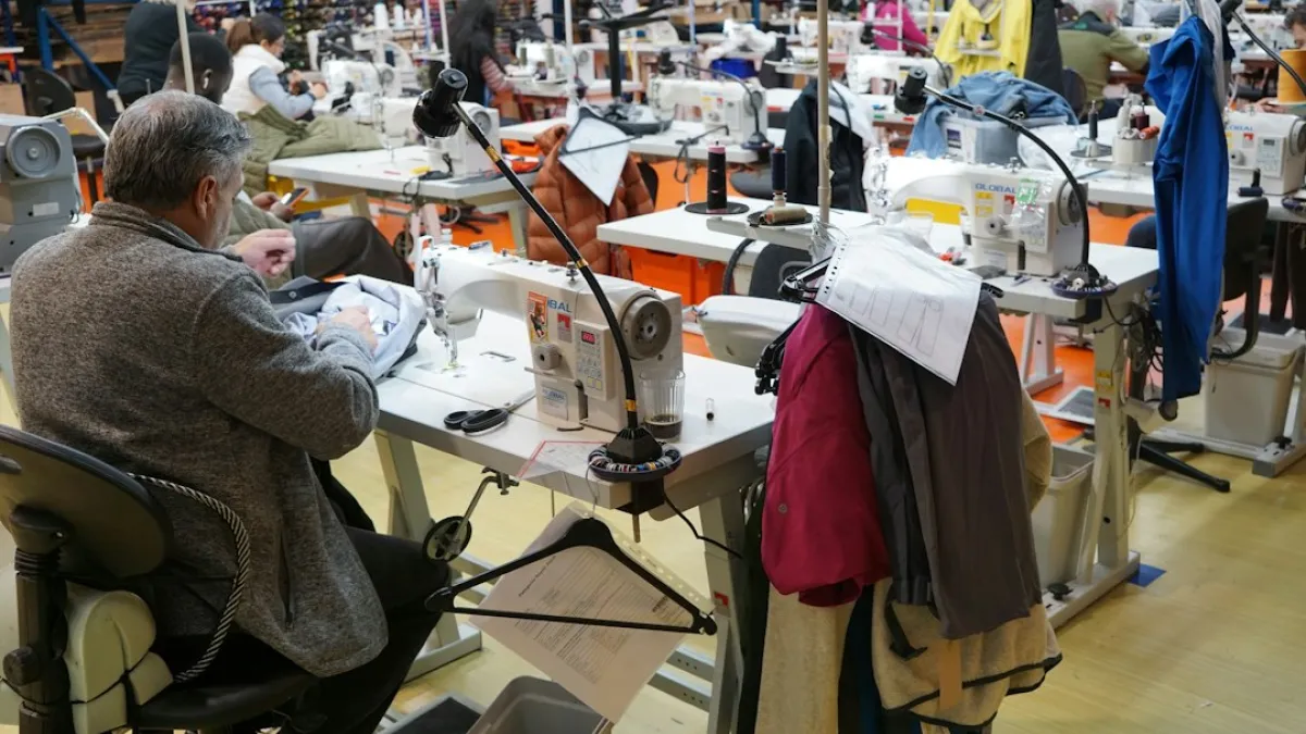 Tailor operating an industrial sewing machine in a clothing repair workshop.