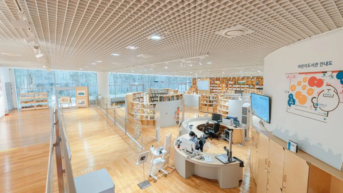Open and airy modern library with bookshelves, desks, and a large screen in a well-lit space.