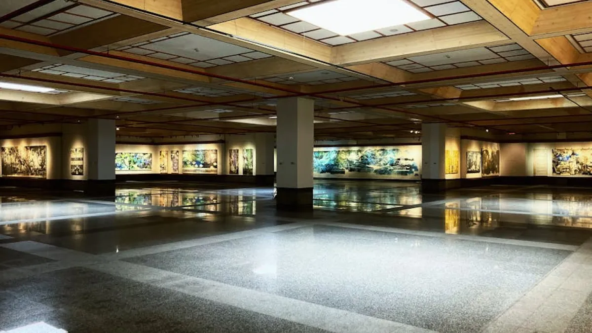 A large, empty art gallery showcasing modern paintings under bright indoor lighting.