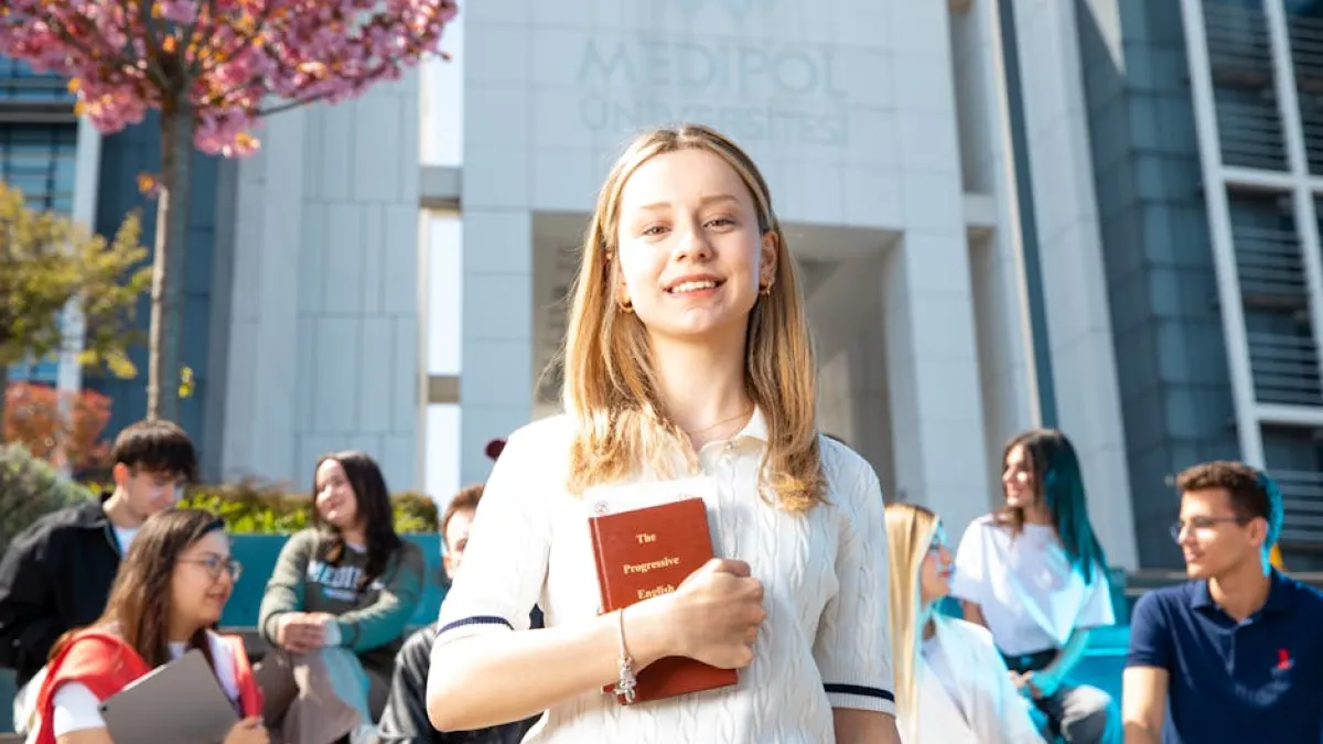 Happy university students socializing on campus, with a focus on a smiling young woman holding a book.