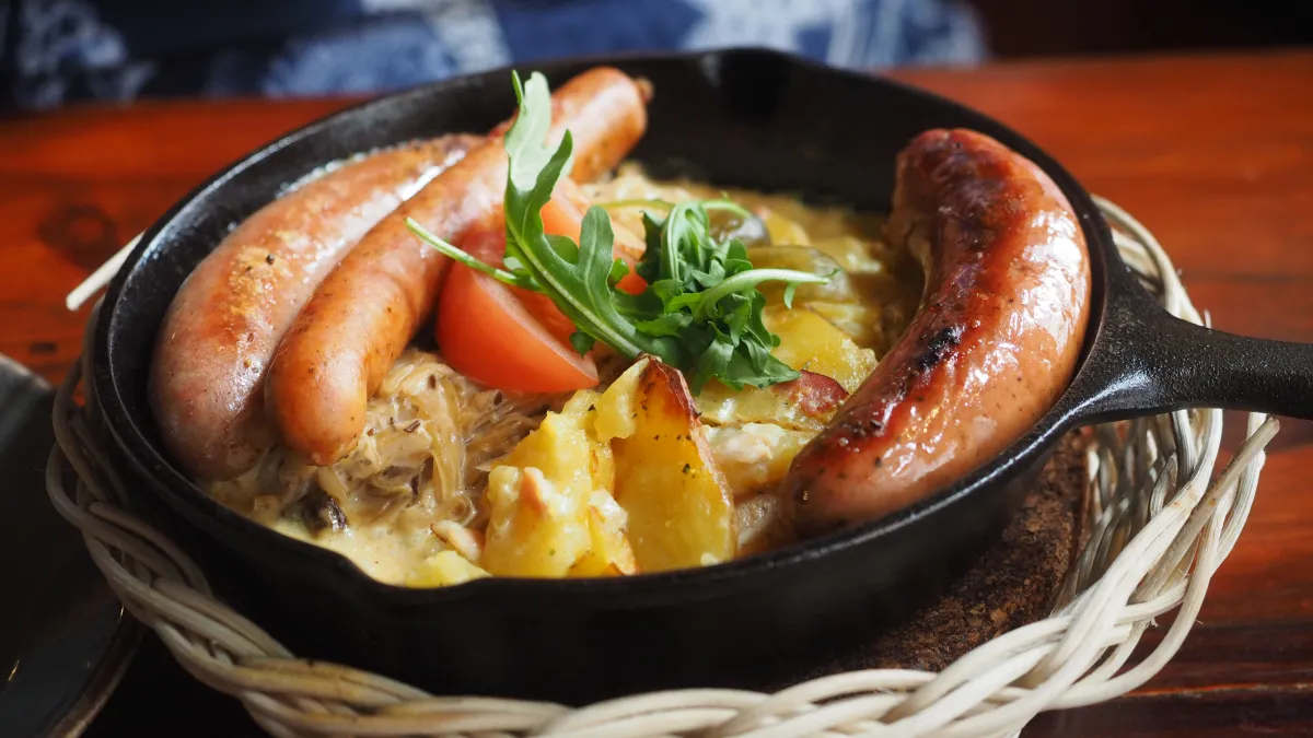 A sausage pan with Thüringer Wurst, Bratwurst, Manchego chili sausage, sour cream sauerkraut, tomato, pickles and bacon cream potatoes served at restaurant Plevna in central Tampere, Finland in June 2025.