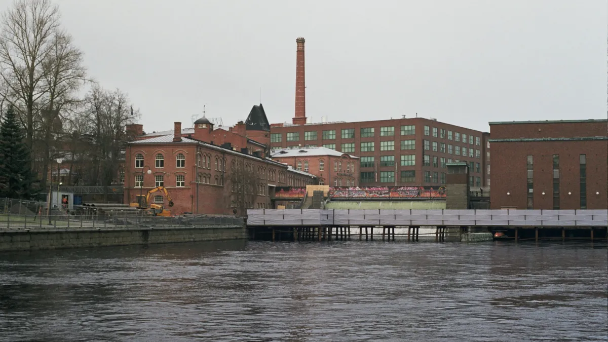 Industrial buildings alongside the Tammerkoski rapids in central Tampere, Finland. On the left are some of the buildings of the former Frenckell paper mill, and behind them is one of the buildings of the former textile factory of Finlayson. On the right is a power plant.