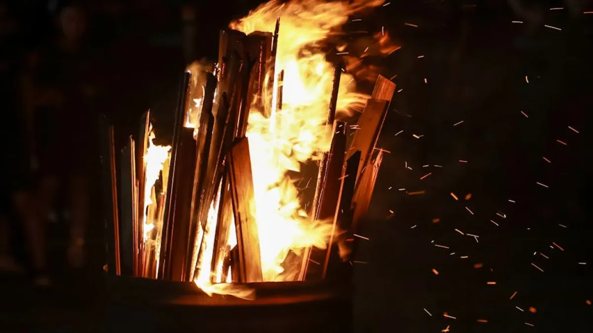 A vivid close-up of wooden planks ablaze in a steel drum, illuminating the night with intense flames.