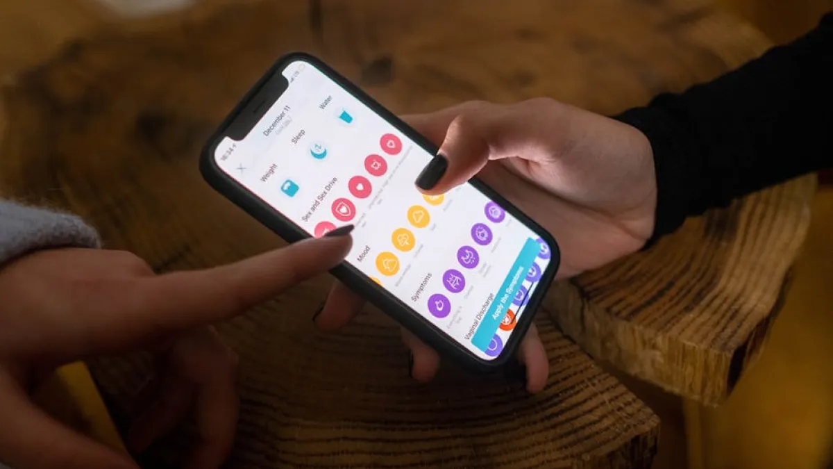 Close-up of hands using a fertility tracking app on a smartphone indoors.