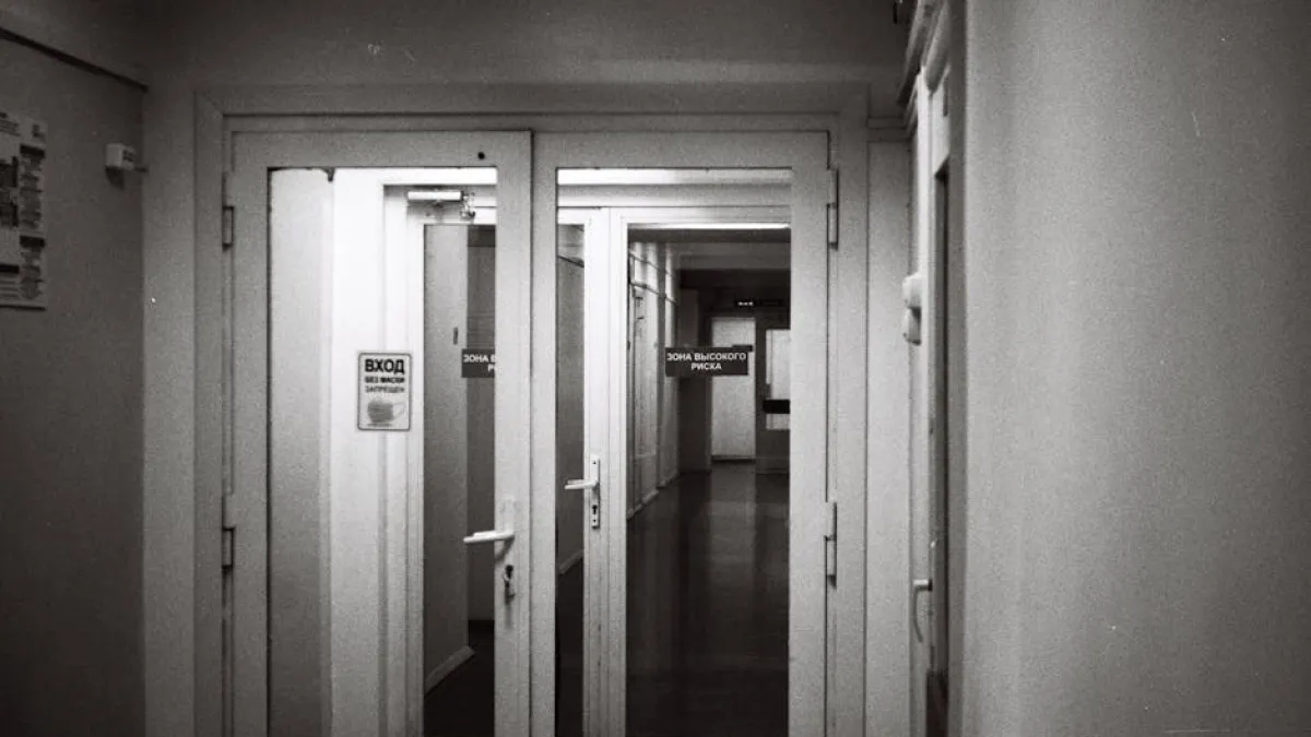 Empty hospital corridor in black and white, emphasizing open doors and healthcare environment.