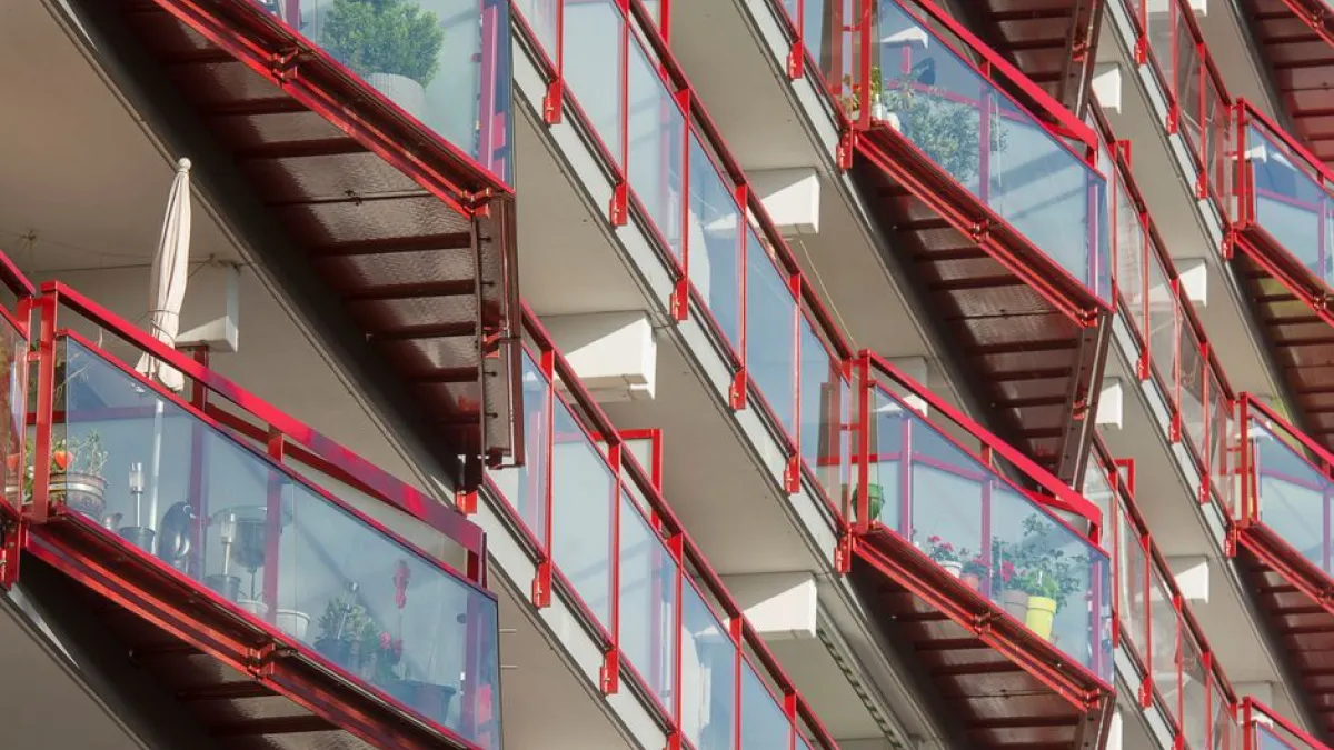 Dynamic view of modern urban apartment balconies featuring red railings and glass panels, showcasing contemporary architecture.